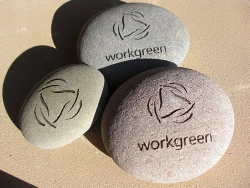 Three stones with the workgreen logo and text, on a sandy surface.