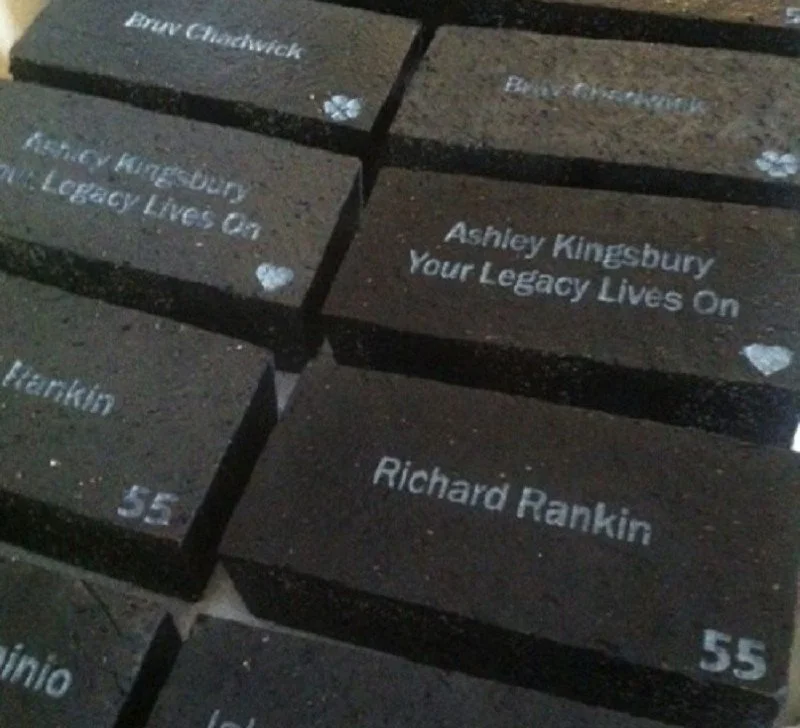 Memorial bricks engraved with names and messages, including "Ashley Kingsbury Your Legacy Lives On" and "Richard Rankin 55."
