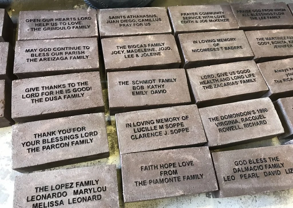 A collection of engraved bricks with various family names and messages, including prayers, memorials, and expressions of gratitude.