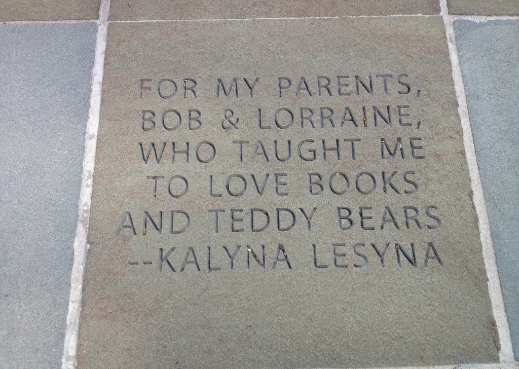 A concrete engraved plaque with a quote dedicated to Kalyna Lesyna, expressing gratitude to her parents Bob and Lorraine for teaching her to love books and teddy bears.