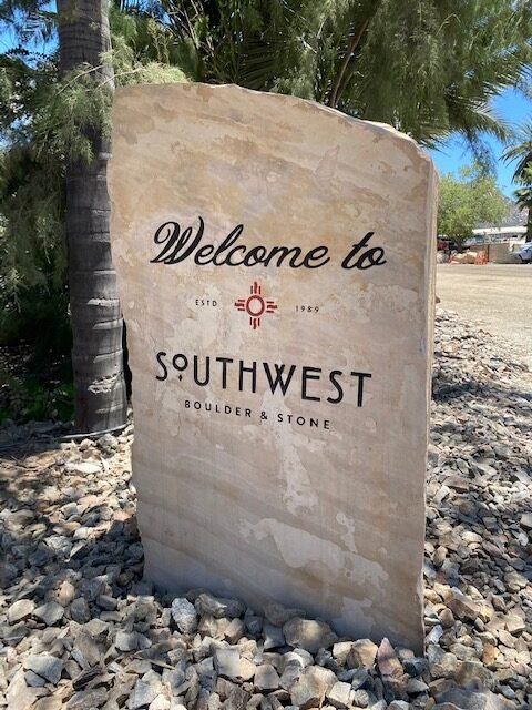 Stone welcome sign for Southwest Boulder & Stone, established in 1989, located outdoors with trees and a parking area in the background.