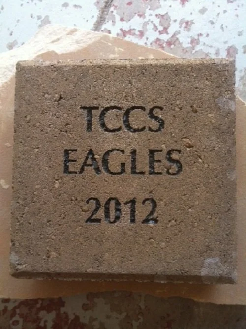 A concrete brick with the engraved text 'TCCS EAGLES 2012' on its front.