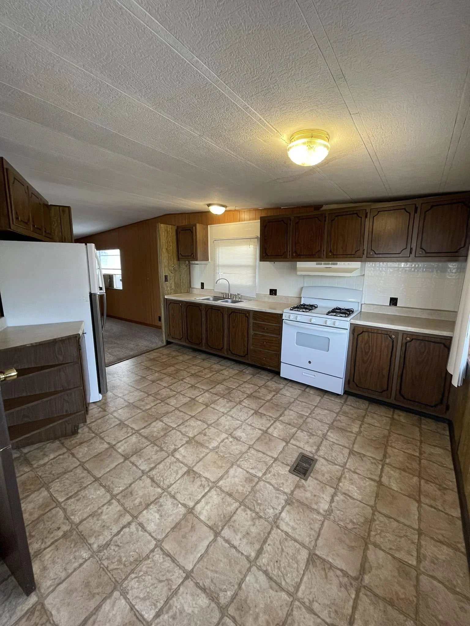 Kitchen with brown wooden cabinets, white stove, white refrigerator, and tiled floor.