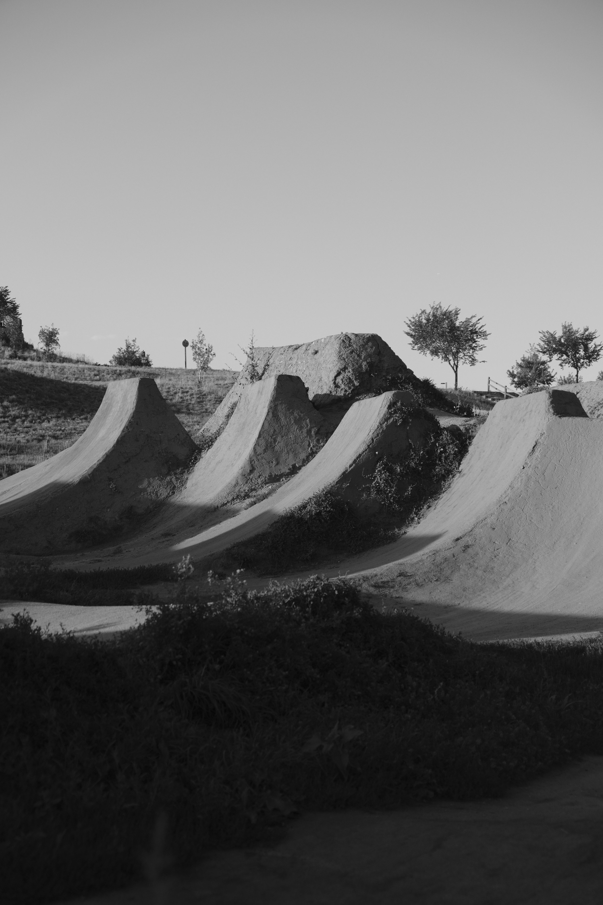 Black and white photo of a skate park with concrete ramps, trees, and a clear sky. Valmont bike park