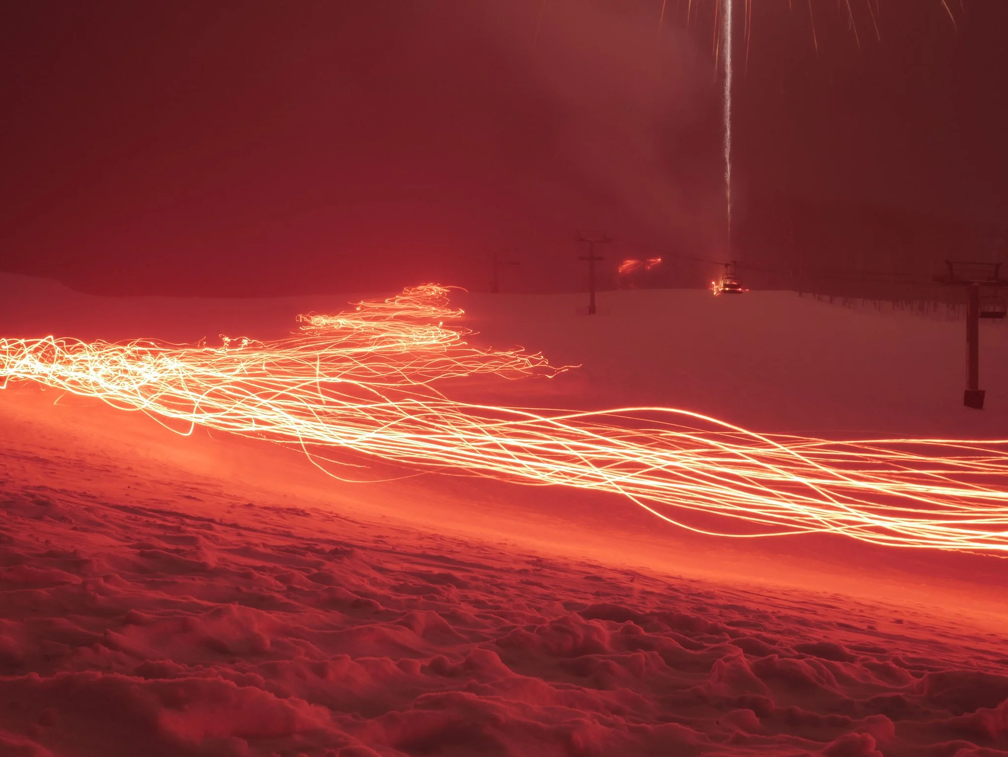 Nighttime scene of a ski slope with bright orange and red light trails from ski or snowboard movements, and equipment such as ski lifts in the background. Crested butte, Christmas Eve, long exposure.