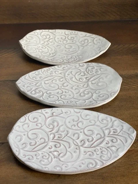 Three white ceramic dishes with intricate swirl patterns, placed on a wooden surface. Sonia Lesage Ceramics