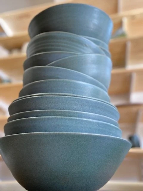 Stacked blue/gray ceramic bowls in a pottery or store display. Sonia Lesage Ceramics