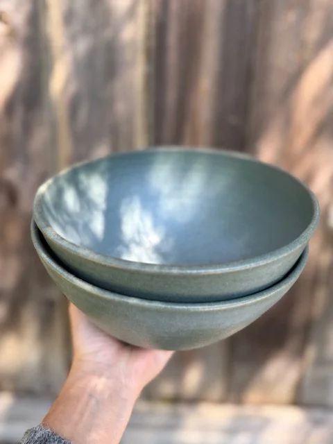 Person holding two blue ceramic bowls outdoors with a wooden fence in the background. Sonia Lesage Ceramics