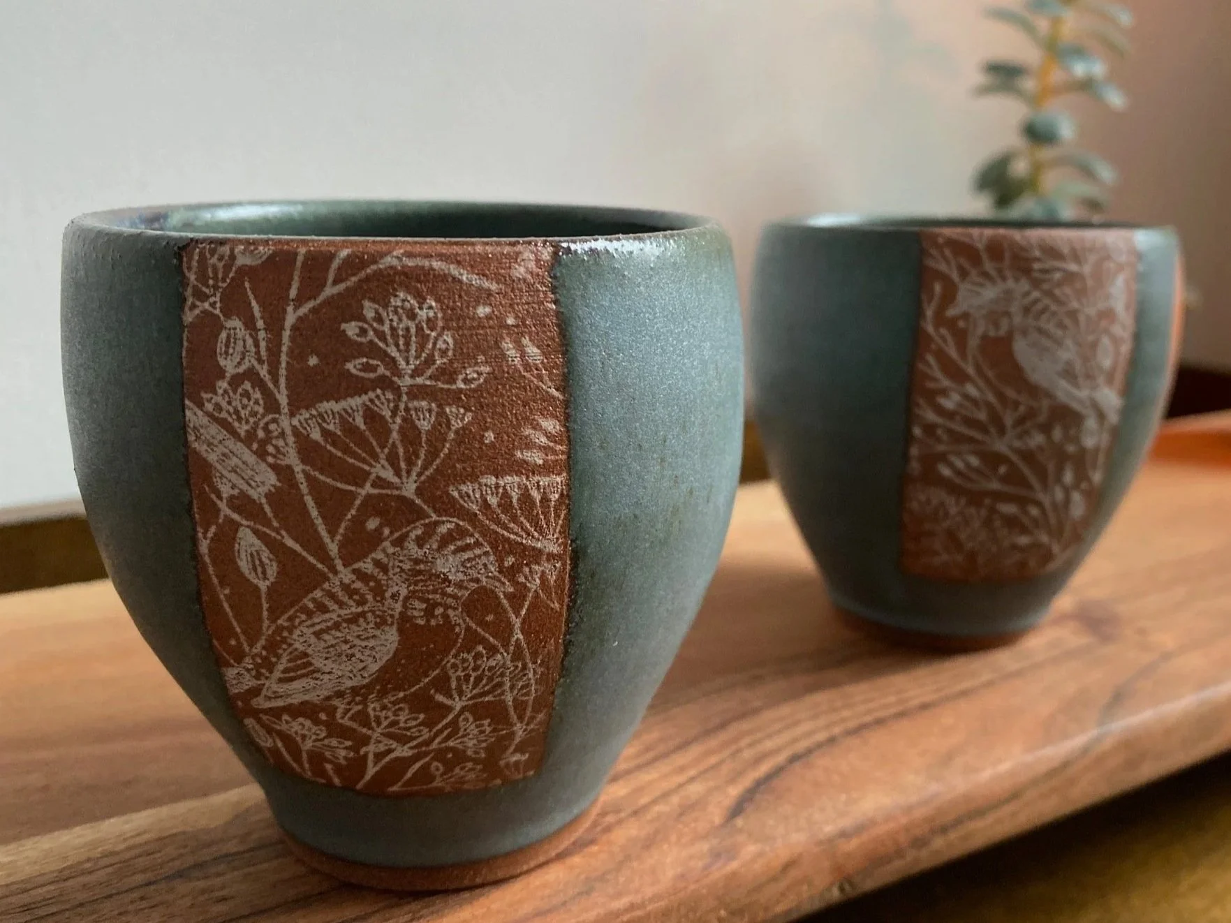 Two ceramic espresso/tea cups with a design of botanical illustrations and birds on a wooden surface. Sonia Lesage Ceramics