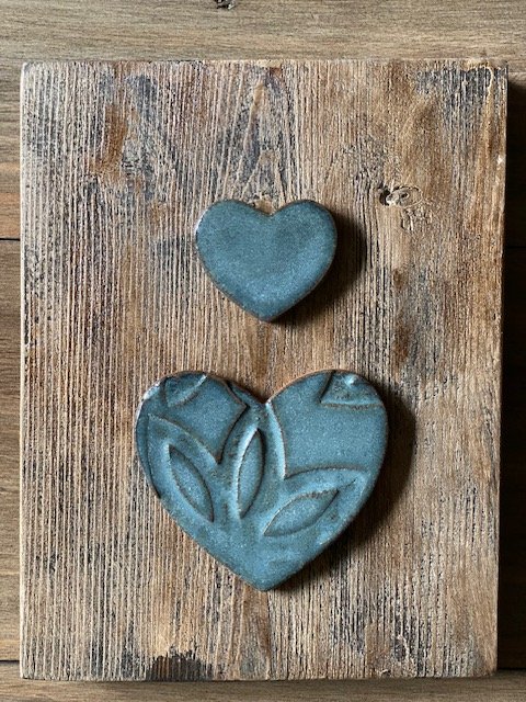 Two blue heart-shaped pottery pieces on a wooden wall hanging.  Sonia Lesage Ceramics