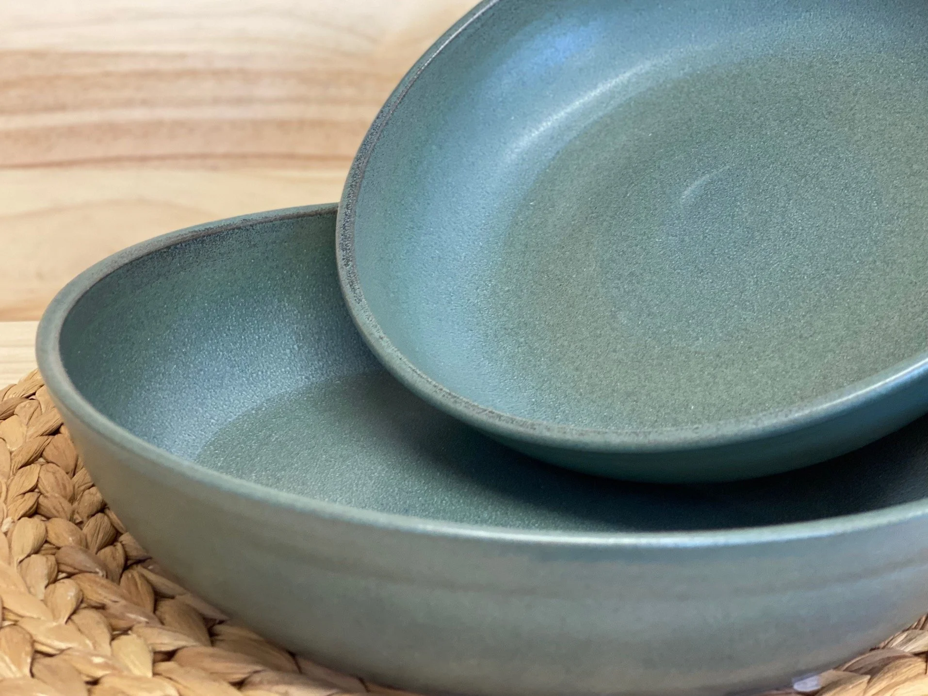 Two stacked blue ceramic plates on a woven placemat with a wooden background. Sonia Lesage Ceramics