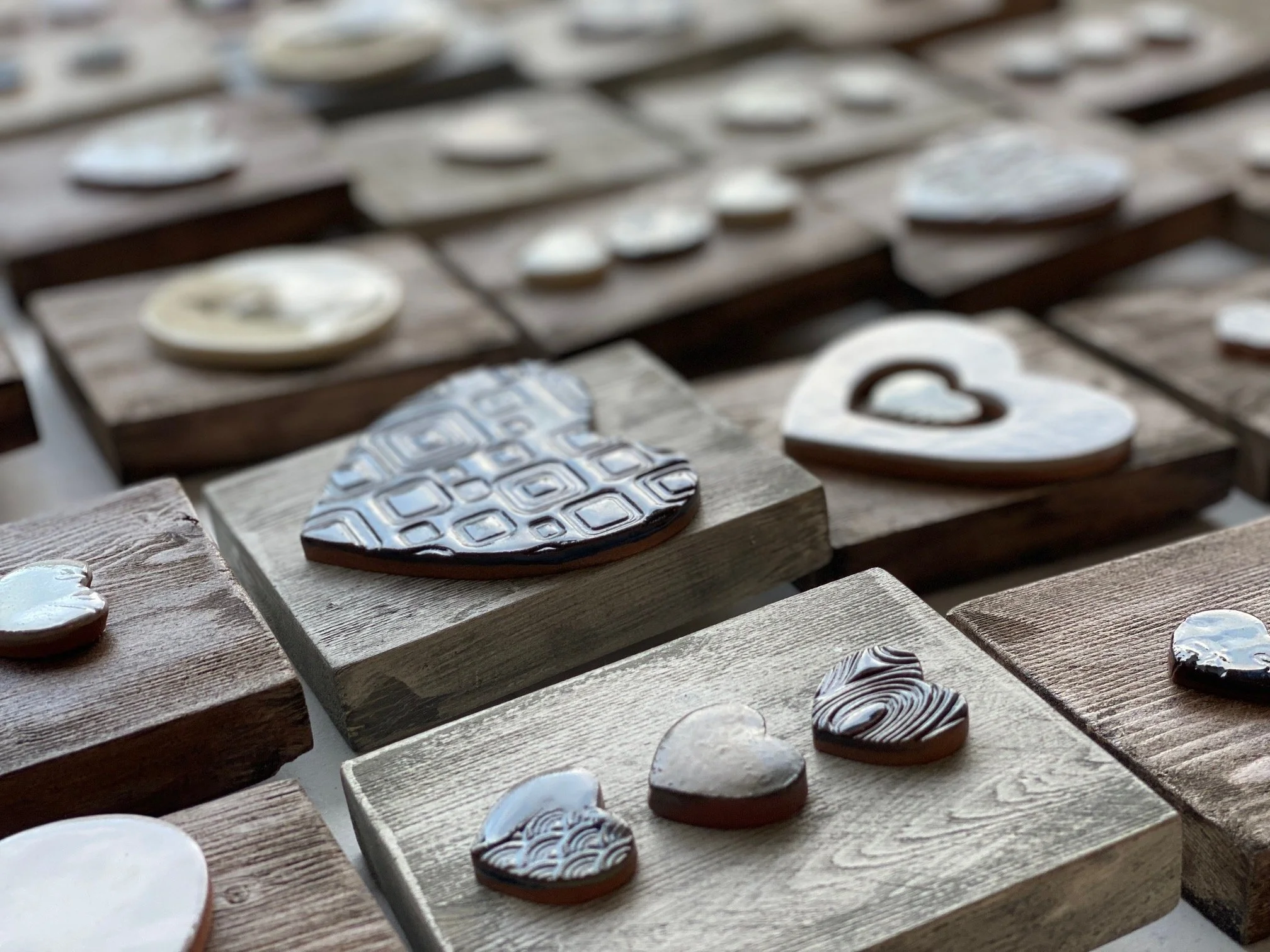 Multiple decorative ceramic hearts on wooden frames, with some featuring geometric patterns and others with swirling designs. Sonia Lesage Ceramics