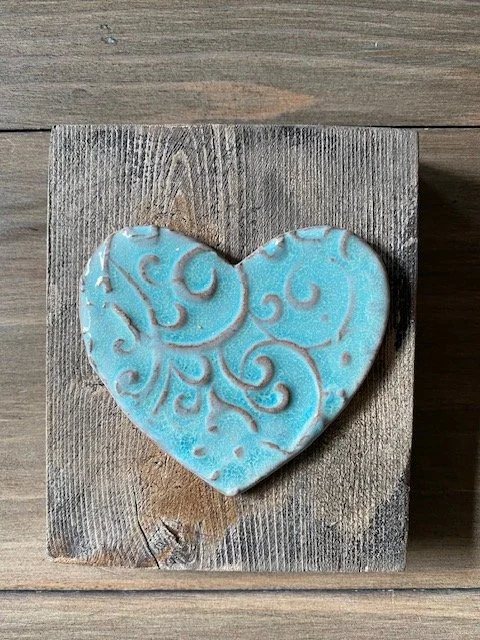 A heart-shaped pottery heart resting on a wooden surface. Wall hanging. Sonia Lesage Ceramics