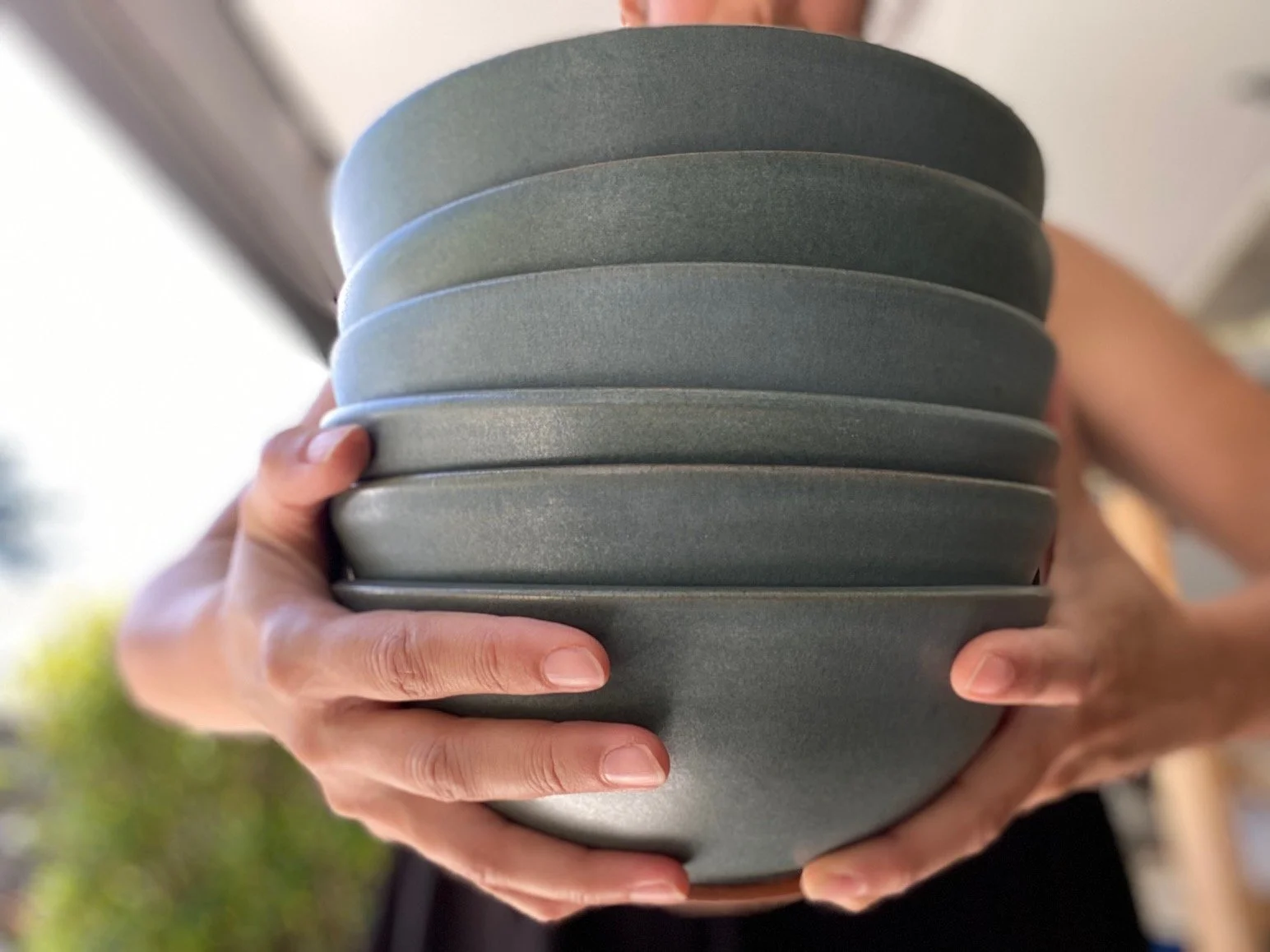 A person holding a stack of blue ceramic bowls. Sonia Lesage Ceramics