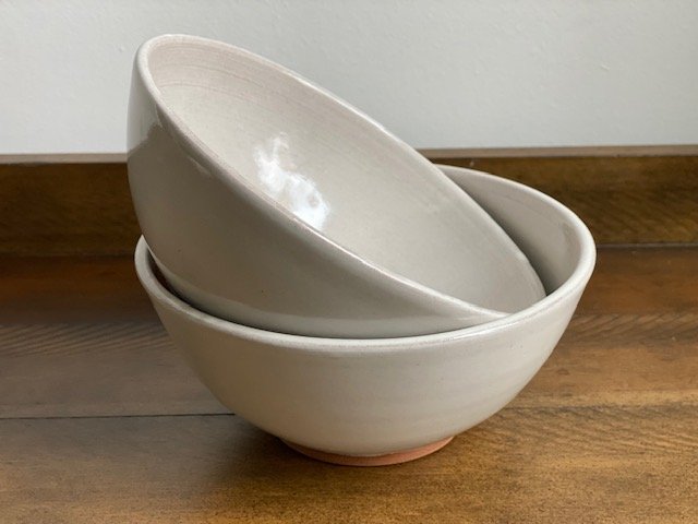 Two stacked white ceramic bowls on a wooden surface. Sonia Lesage Ceramics
