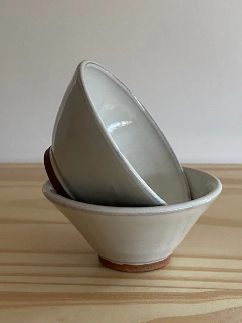 A set of two stacked white ceramic bowls on a light wooden surface. Sonia Lesage Ceramics