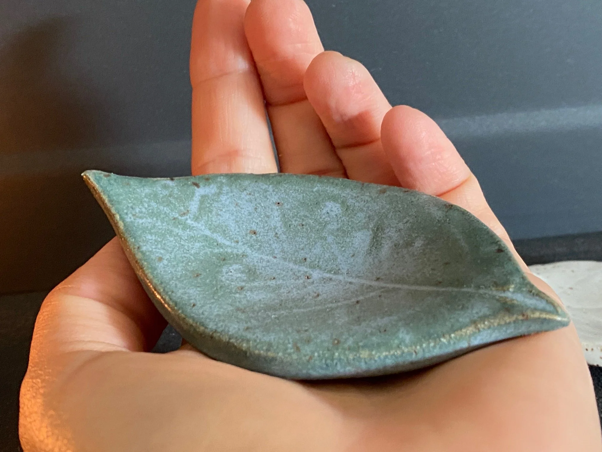 A person's hand holding a ceramic tea light holder shaped like a leaf with a blue glaze. Sonia Lesage Ceramics