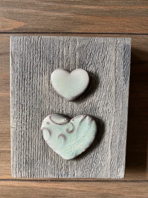 Two heart-shaped ceramic hearts with a swirling pattern, placed on a wooden wall hanging. Sonia Lesage Ceramics.