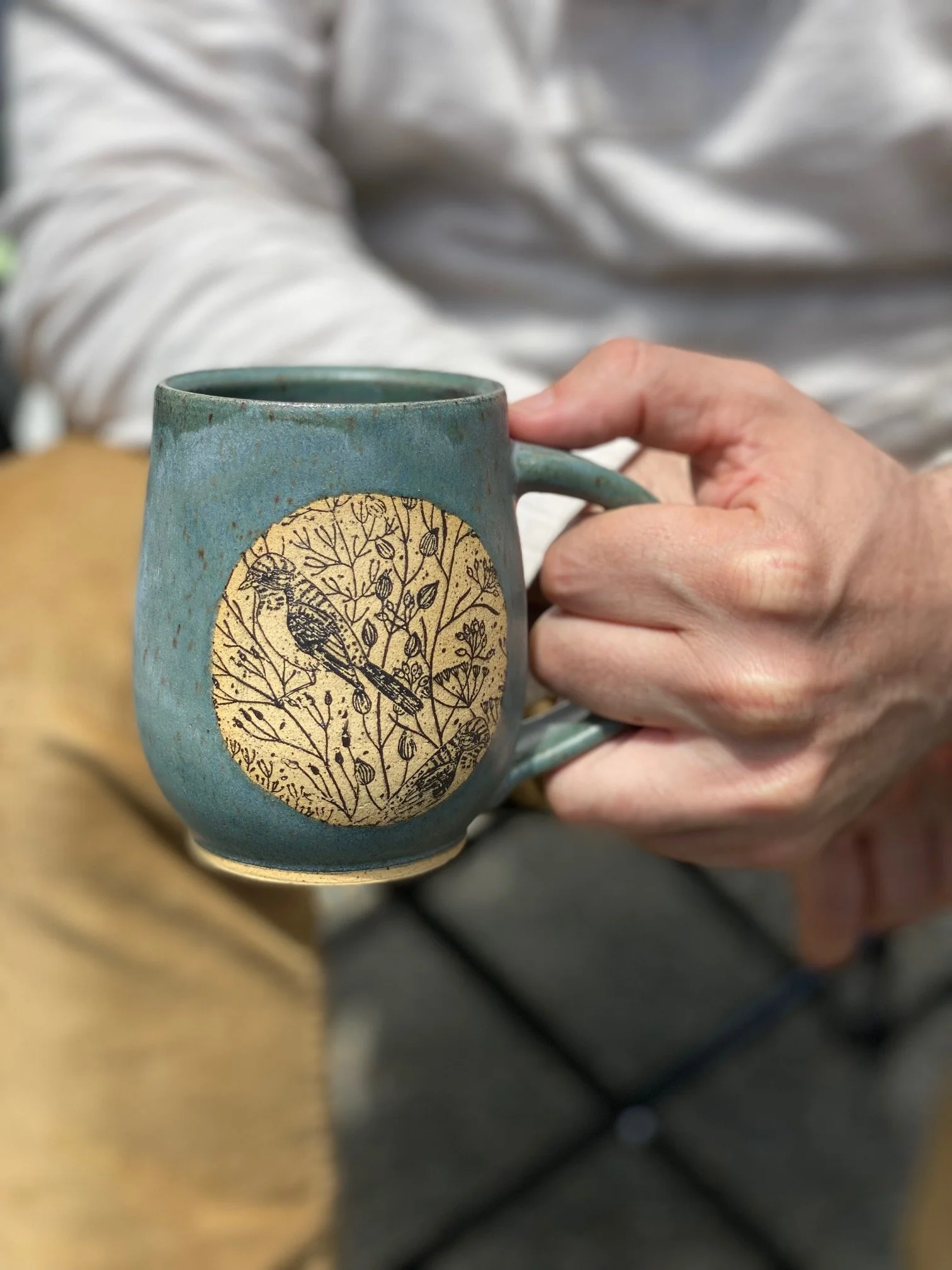 A person holding a blue ceramic mug with a bird illustration inside a circle on its surface. Sonia Lesage Ceramics