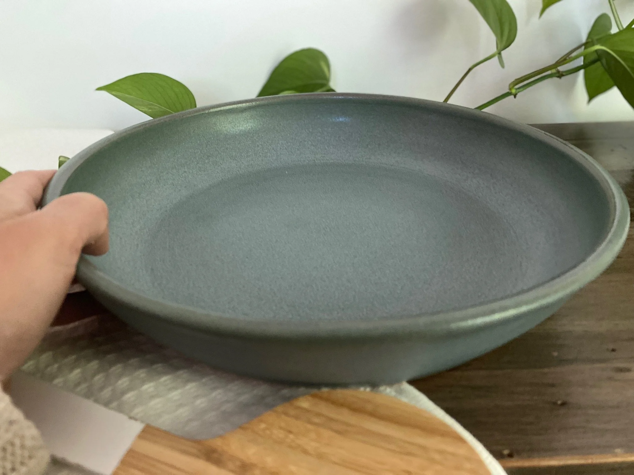 A person holding a large, blue ceramic  platter in front of a background with green plant leaves. Sonia Lesage Ceramics