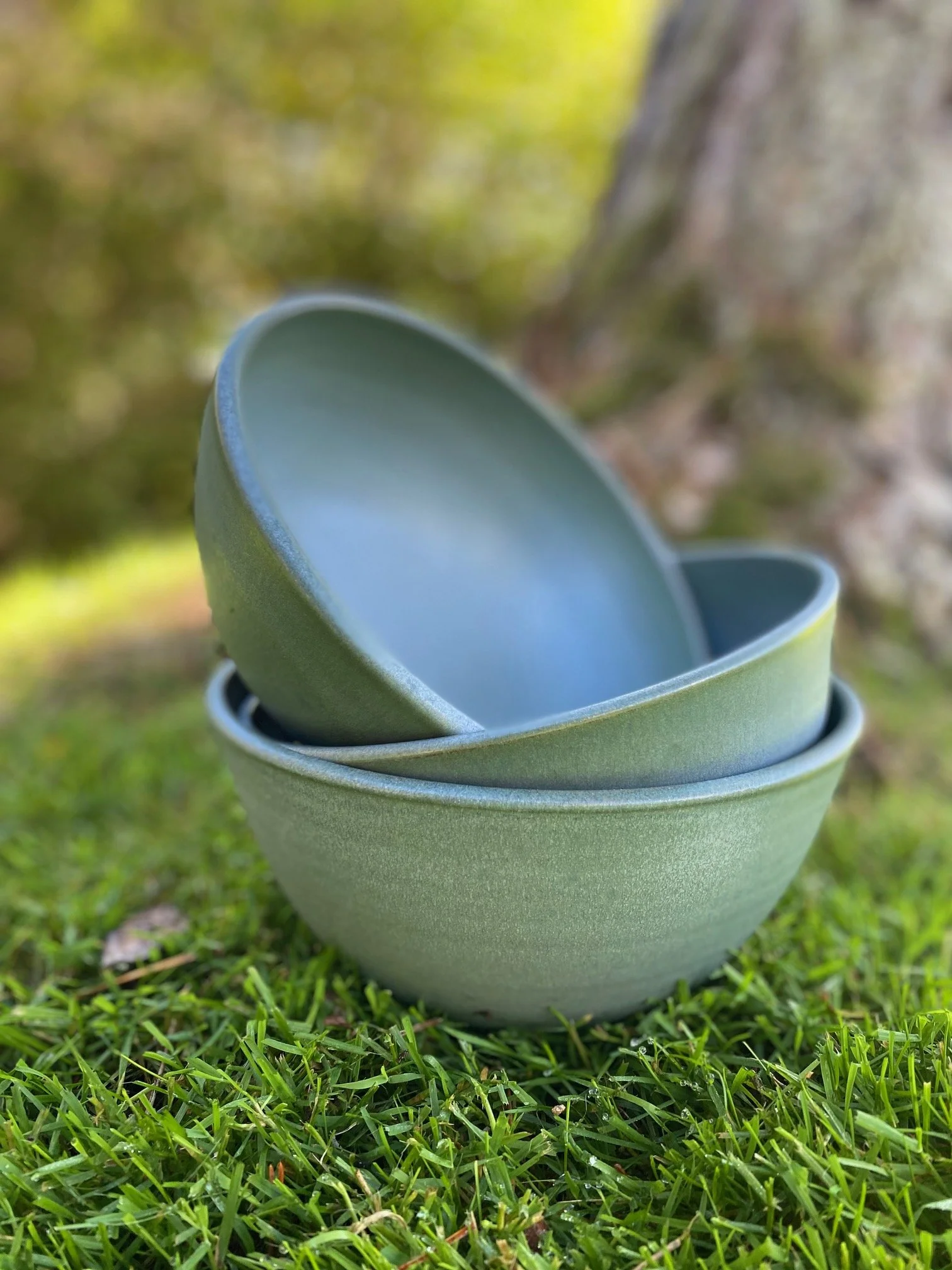 Stack of three blue/grey ceramic bowls on the grass with a blurred natural background. Sonia Lesage Ceramics
