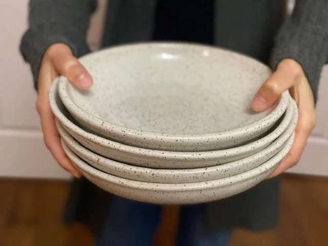 Person holding four stacked white speckled ceramic plates. Sonia Lesage Ceramics