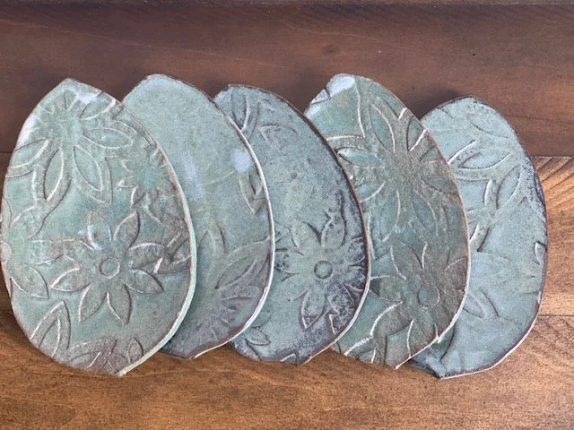 Collection of five decorative leaf trinket plates with floral patterns, arranged in a row on a wooden surface. Sonia Lesage Ceramics