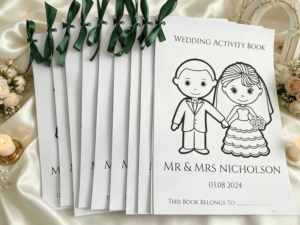 Wedding activity book for Mr. & Mrs. Nicholson, featuring a cartoon illustration of a bride and groom holding hands, on satin fabric surrounded by flowers and candles.