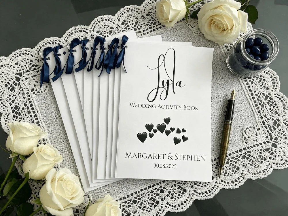 Wedding activity book placed on a lace doily with white roses, blue ribbons and a pen.