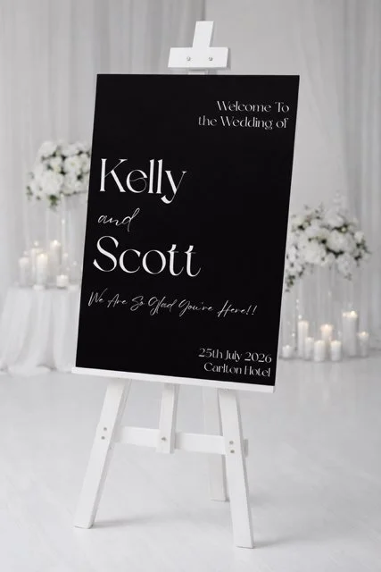 Wedding welcome sign on an easel with white flowers and candle decorations in the background.