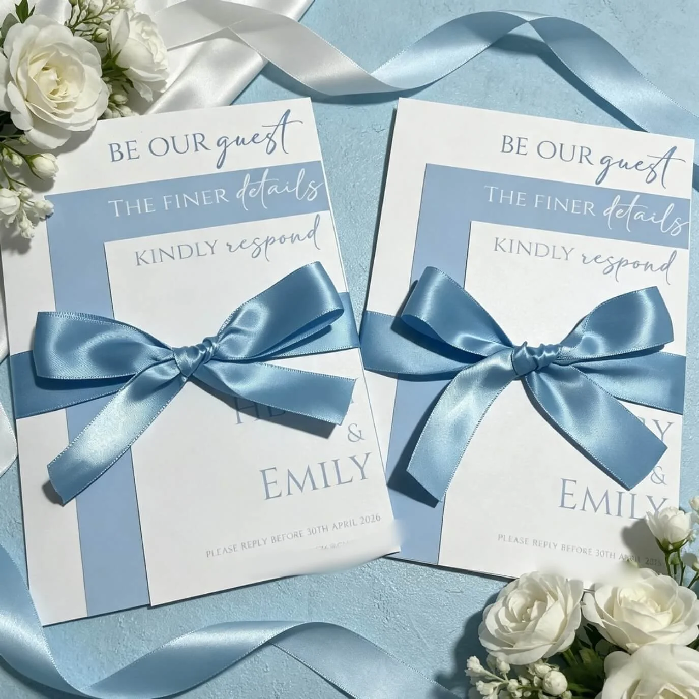 Two wedding invitations with blue ribbons, white flowers, and light blue textured background.