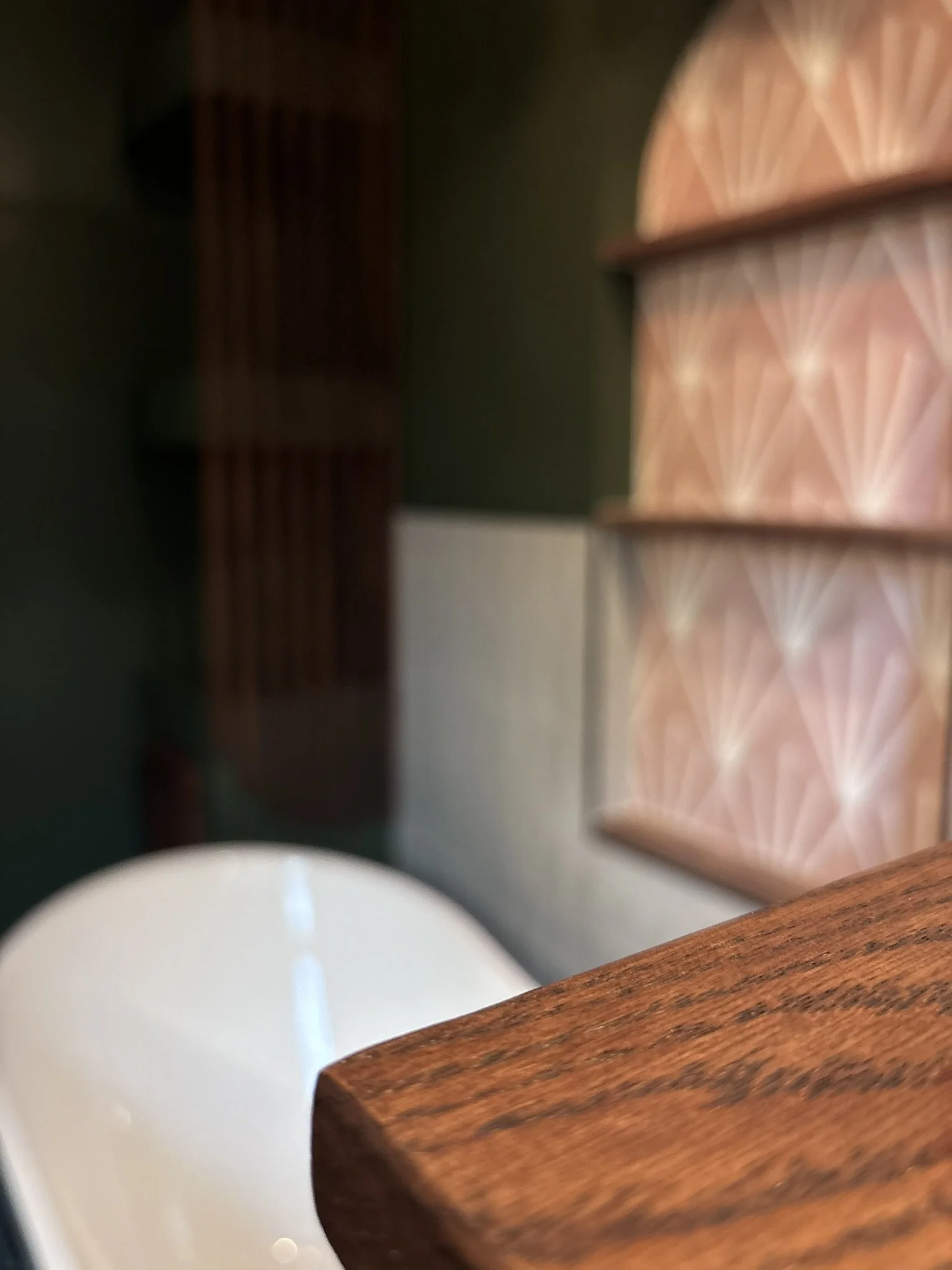 Close-up of a wooden table edge in a room with patterned wallpaper and furniture, with a blurred background.