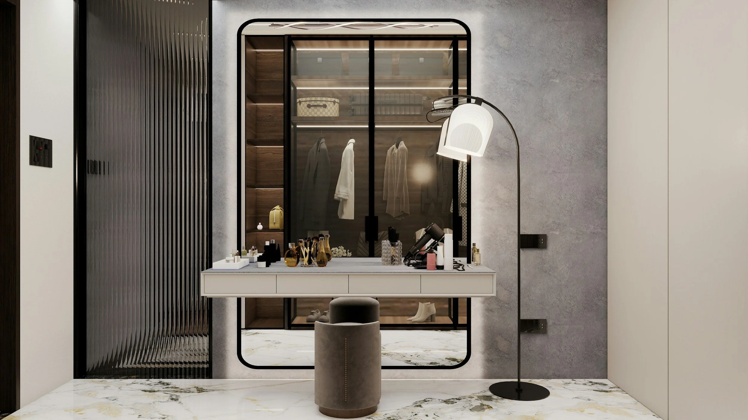 Modern dressing area with a white vanity table, various cosmetics, perfume bottles, and a mirror. Behind the table is a glass wardrobe with hanging clothes and shelves, flanked by textured wall panels. A gray upholstered stool and a contemporary floor lamp are also present.
