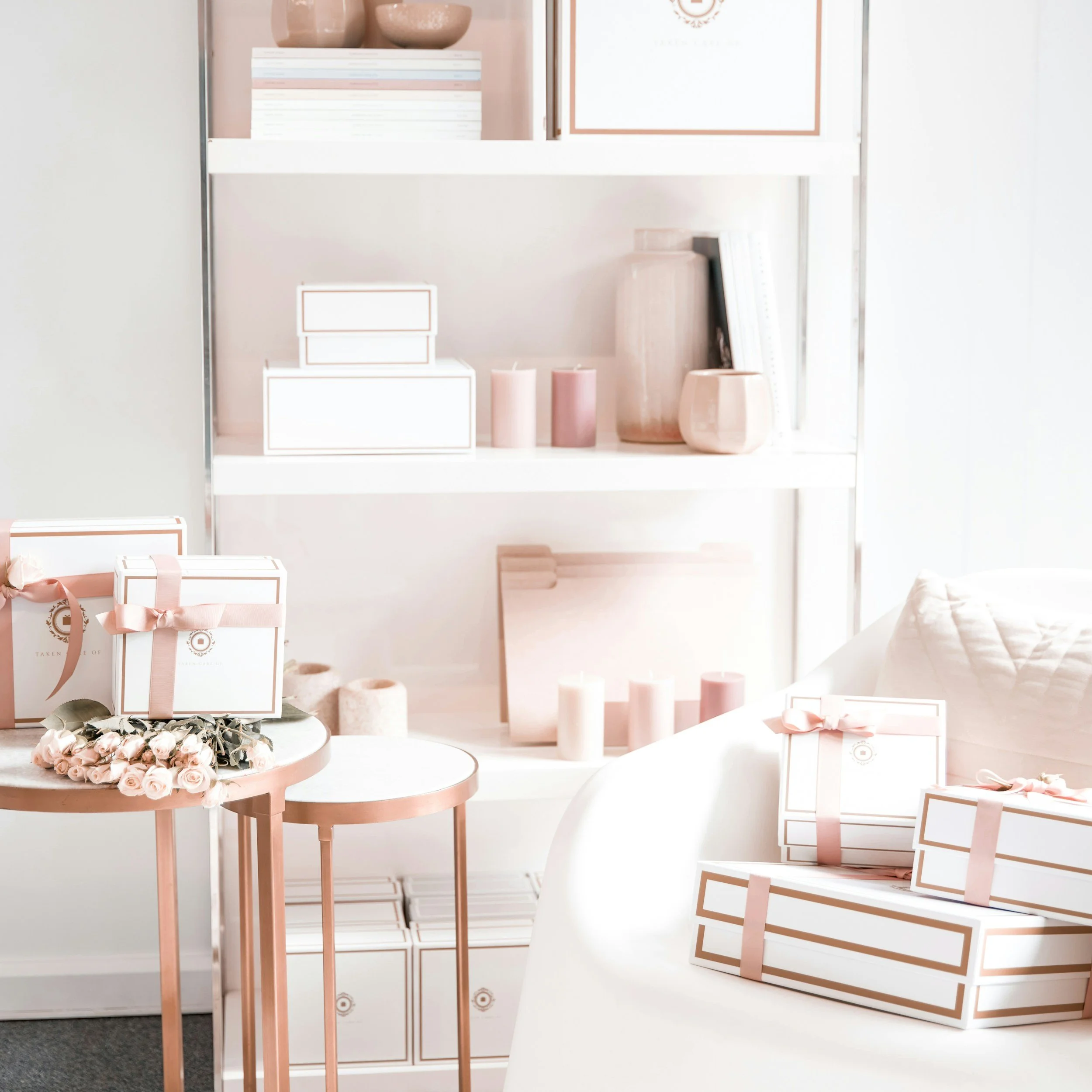 Decorative pink and white gift boxes, candles, and vases on a white table and shelves in a bright, modern room.