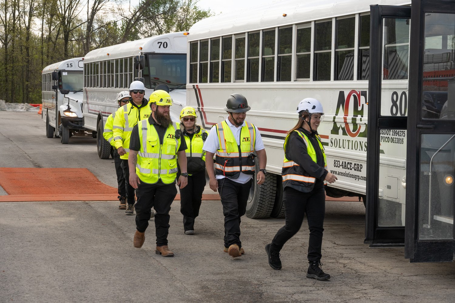 Group of people wearing safety vests and helmets walking near a bus on a construction site.