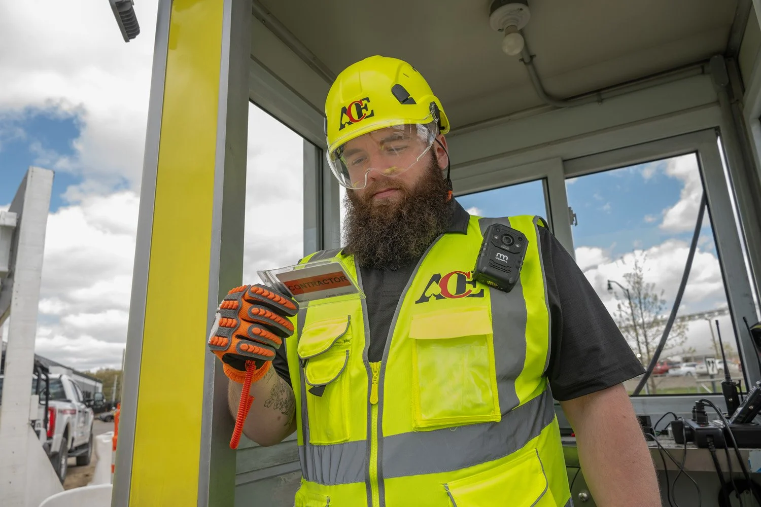 Construction worker in safety gear, high-visibility vest and helmet, looking at a tablet with a 'Contractor' badge, inside a construction site.