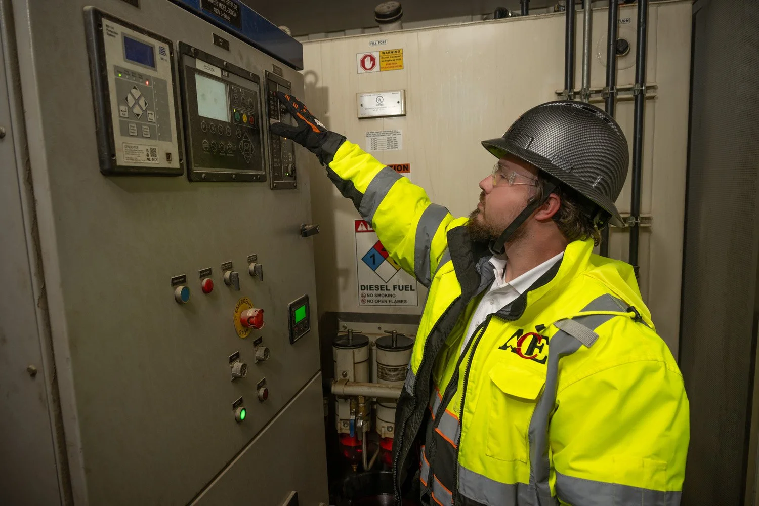 A man wearing safety glasses a black helmet and a bright yellow safety jacket operating a control panel in an industrial setting.