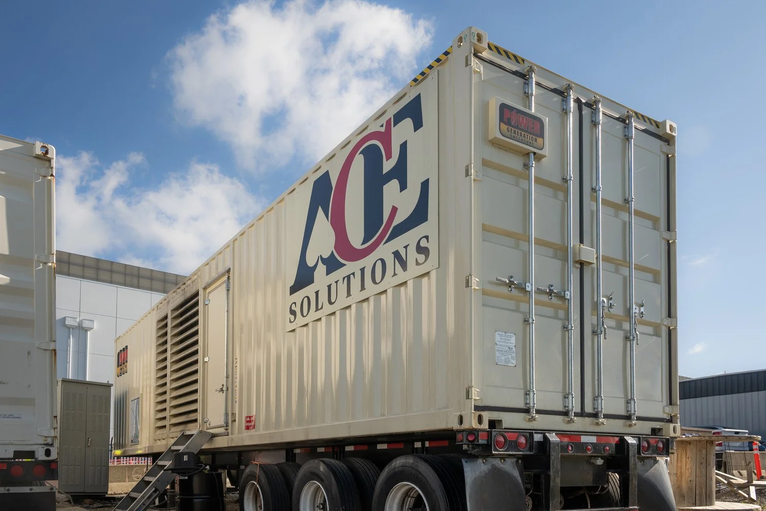 A beige mobile generator trailer with the logo 'ACE Solutions' displayed on the side, parked outdoors under a blue sky with clouds.