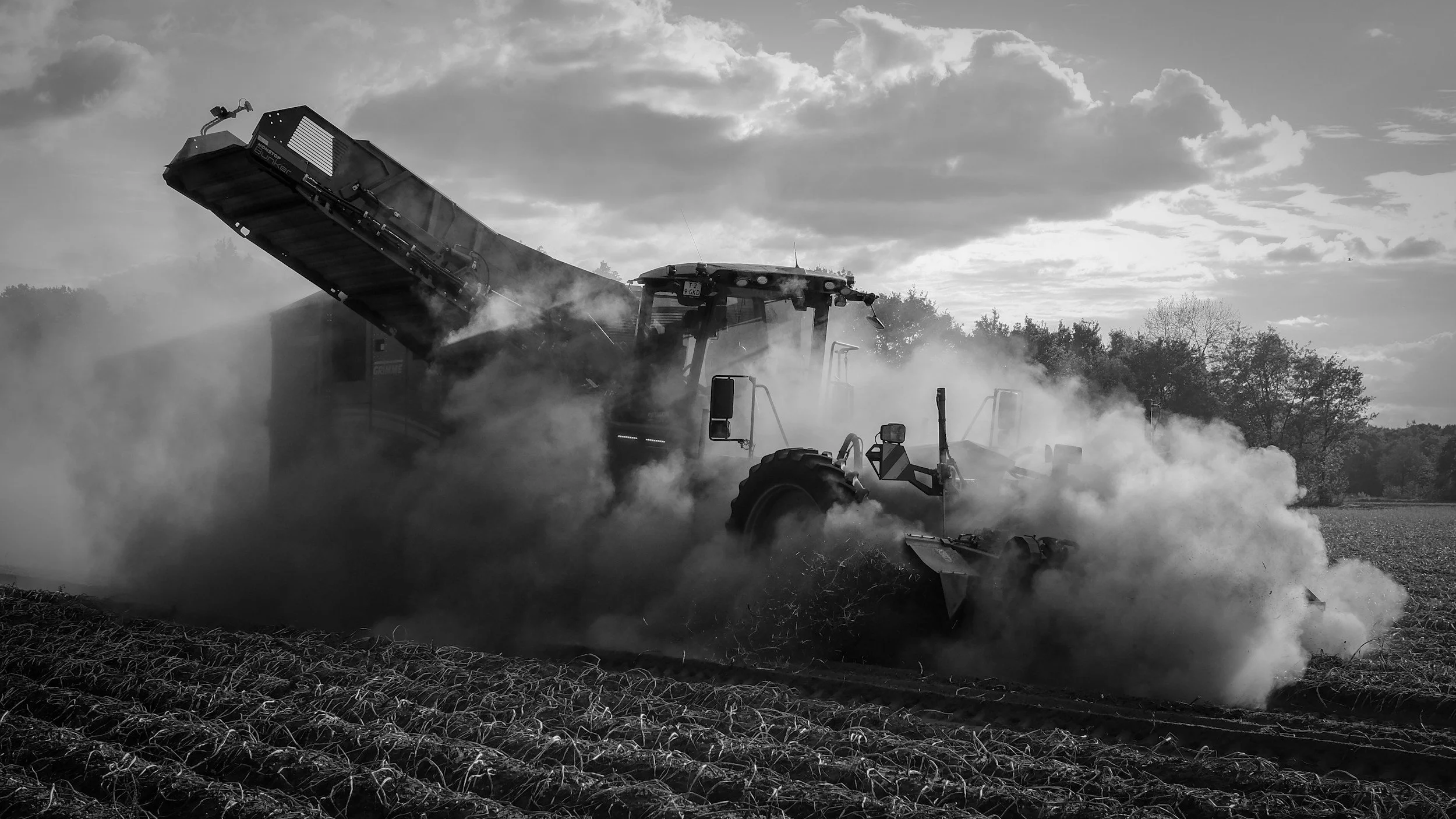 A large tractor in a field with dust and smoke around it, working on the soil.