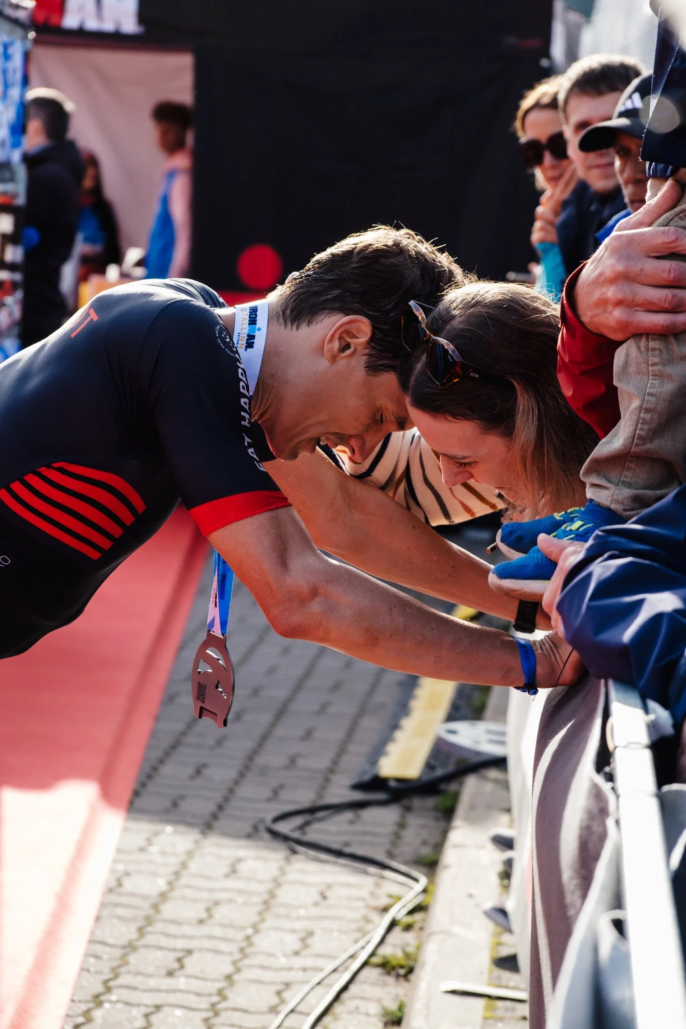 Ein männlicher Athlet nach einem Wettkampf erhält eine Medaille. Er ist müde und lächelt, während er von einer Frau und anderen Menschen begrüßt wird.