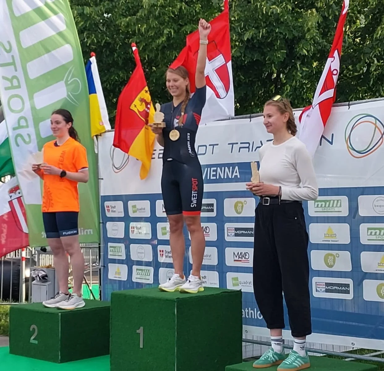 Siegerin auf dem ersten Platz bei einer Siegerehrung im Sport, die Medaille um den Hals, das Trikot im deutschen Design, bei einer Veranstaltung in Wien, Österreich, mit Landesflaggen im Hintergrund.