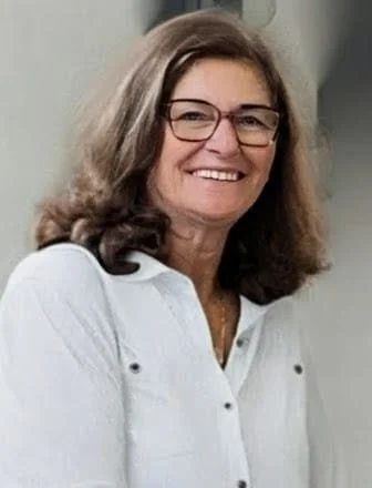 A woman with shoulder-length brown hair and glasses, smiling, wearing a white shirt.