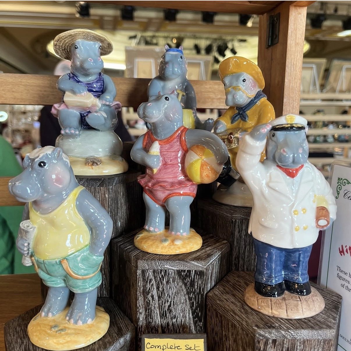 Collection of ceramic animal figurines dressed as humans, displayed on wooden stands, resembling a beach or vacation scene.