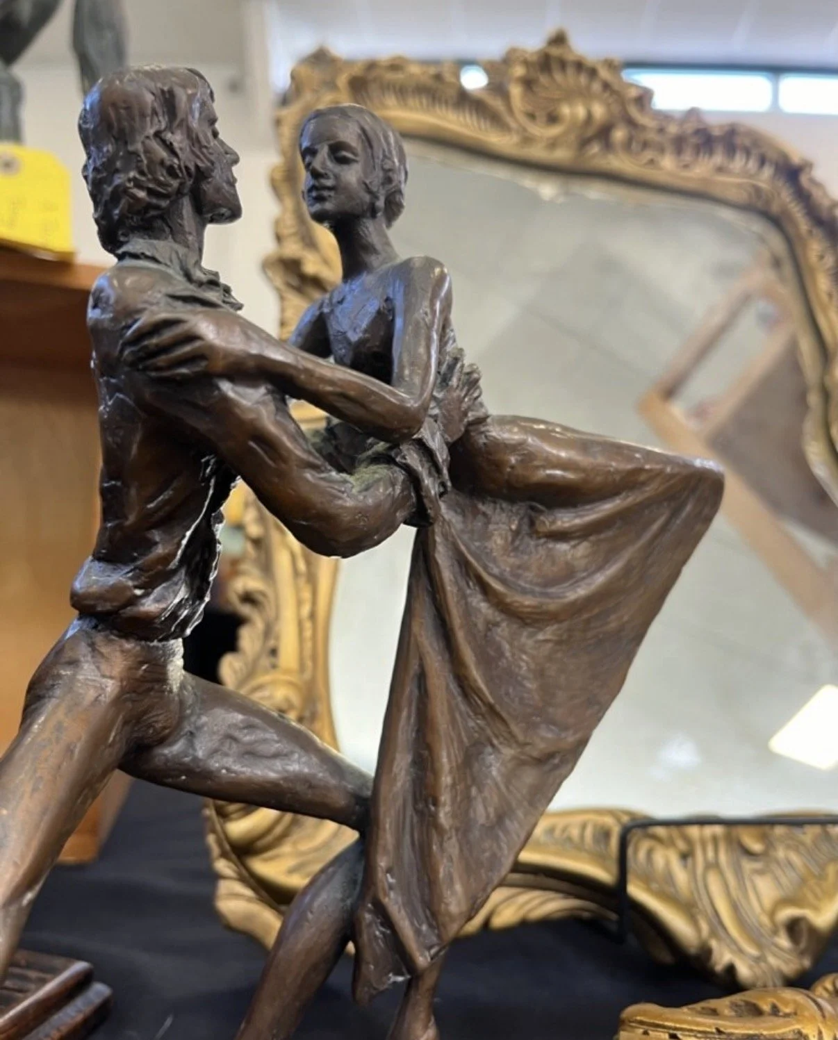Bronze sculpture of a man and woman dancing closely, with a large ornate mirror in the background.