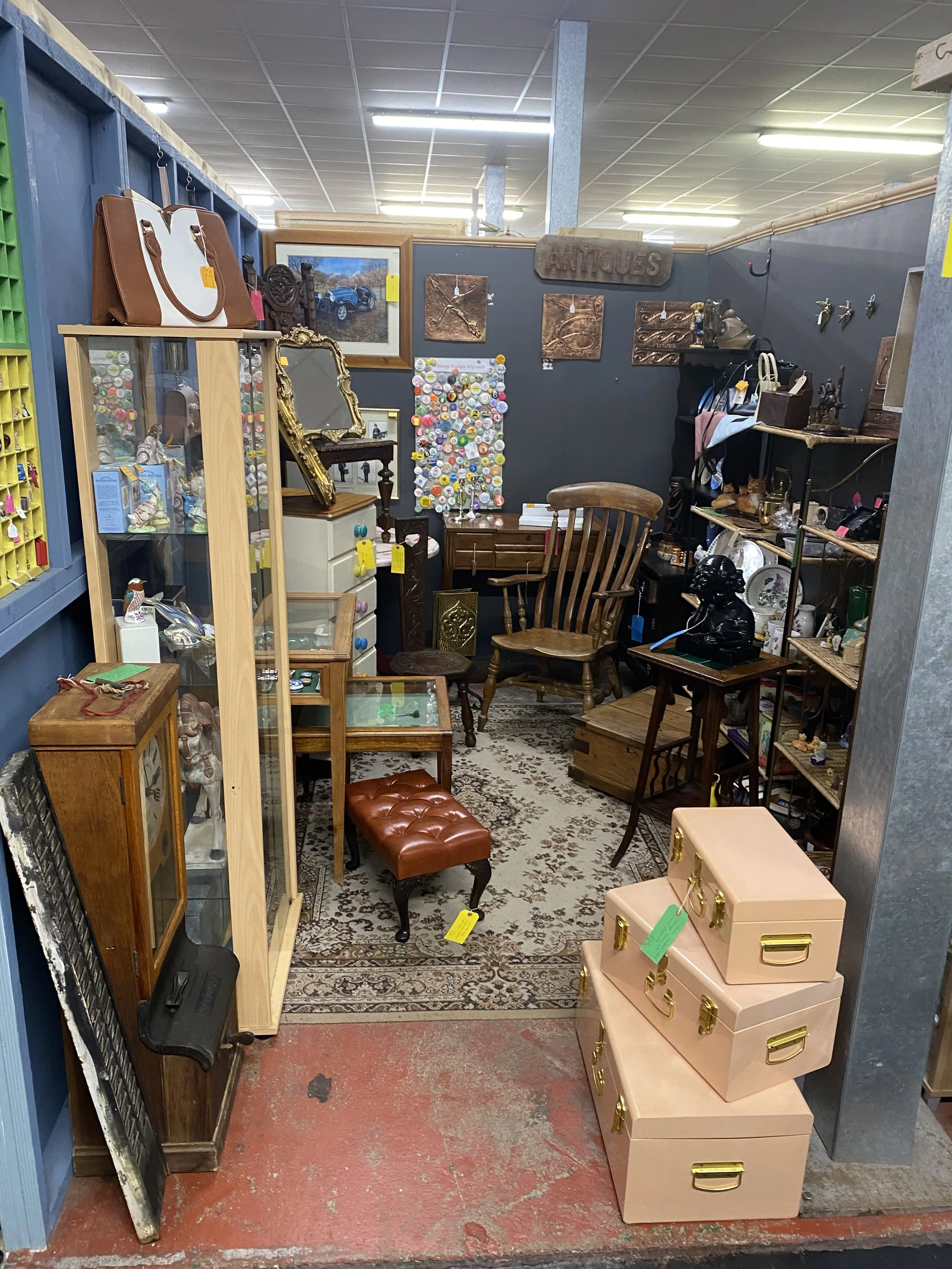 An antique shop filled with various vintage items, including picture frames, pottery, jewelry, lamps, and furniture, arranged on shelves and tables.