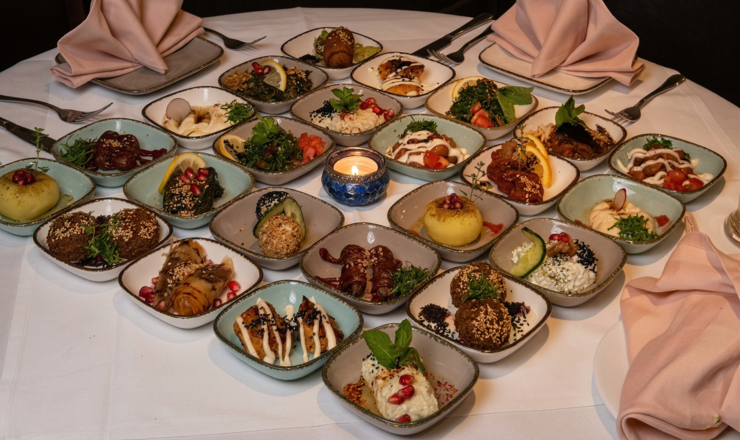 Ein Tisch mit mehreren kleinen Schalen voller verschiedener orientalischer oder mediterraner Vorspeisen und Häppchen, dekoriert mit Zitronenscheiben, Kräutern und Granatapfelkernen.