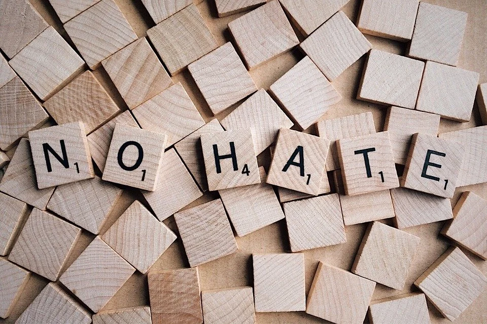 Scrabble tiles spelling out 'NO HATE' on a scattered wooden surface.