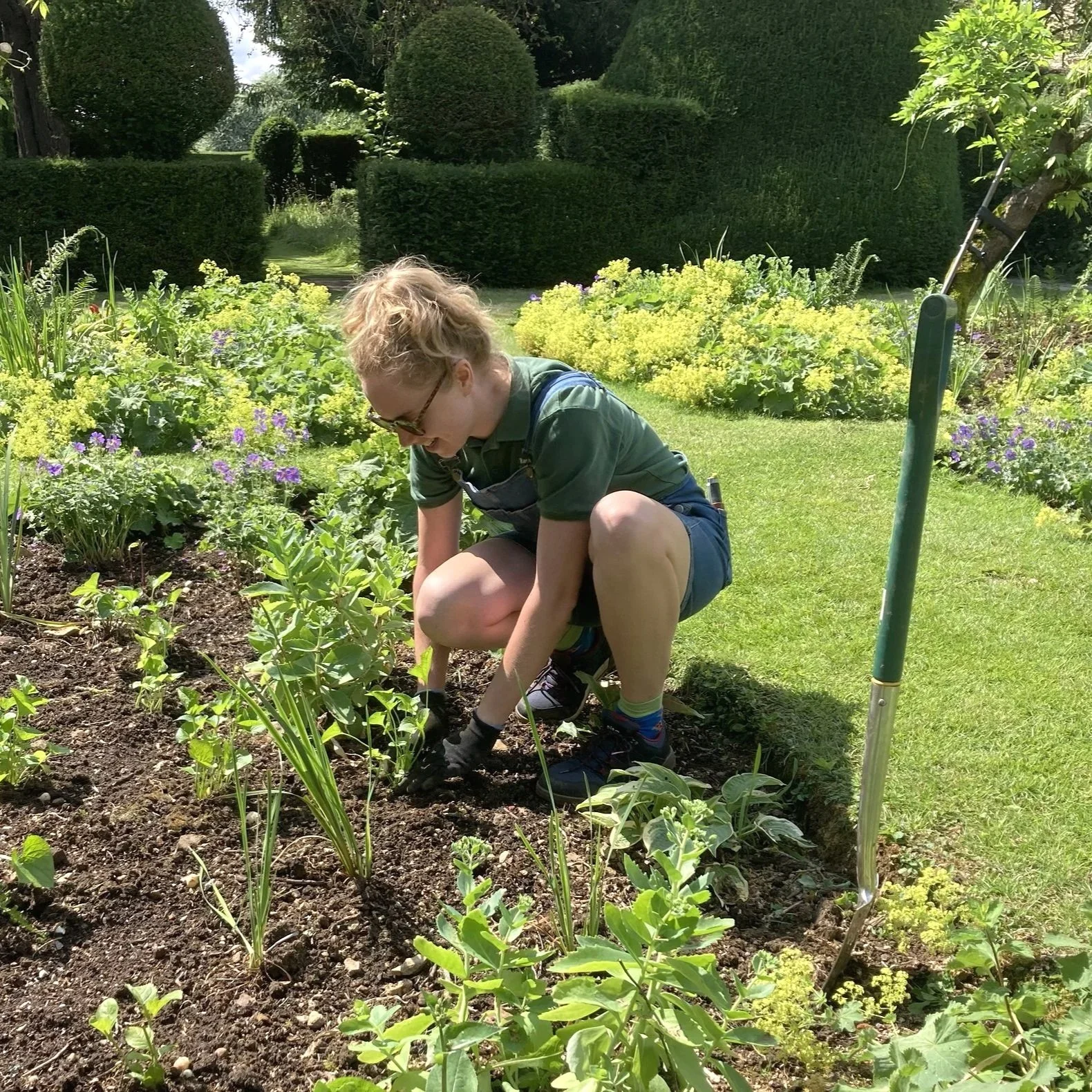 Emily, The Gloucestershire Gardener, crouched down and planting up a bed in a Cotswold garden.