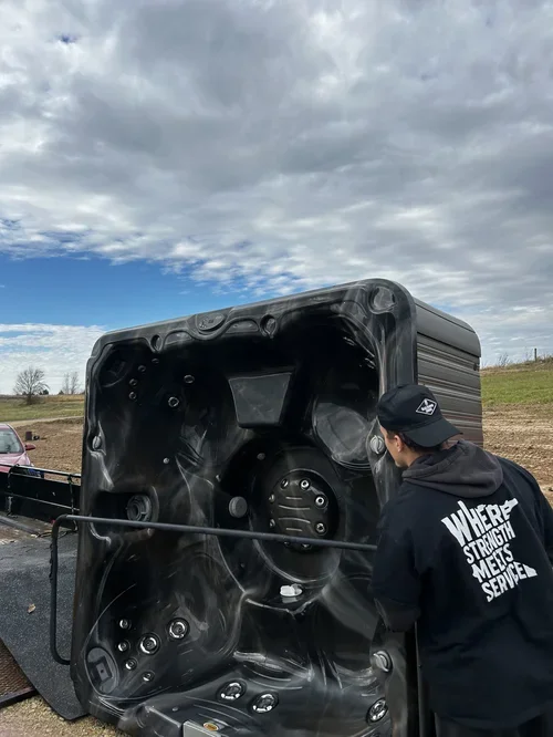 Person inspecting a hot tub laid on its side outdoors on a cloudy day.
