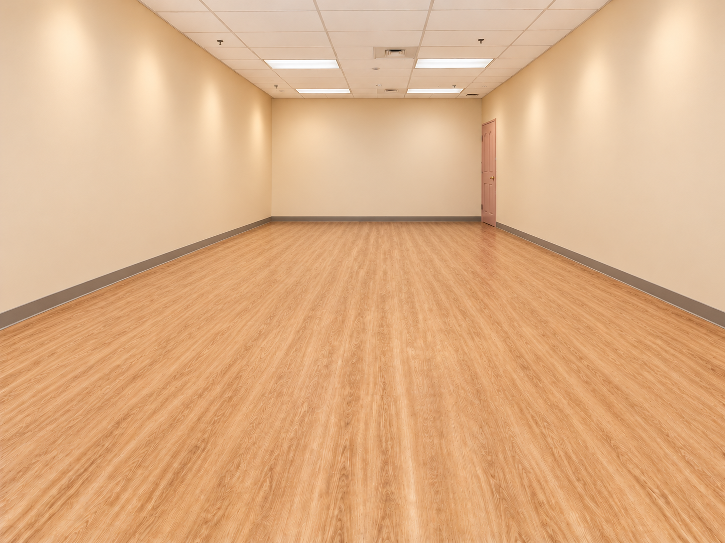 Empty room with beige walls, a beige ceiling, and wooden flooring. There is a closed door on the right side of the room.